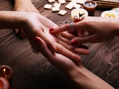 A psychic holds a persons hand and points to the life line on their palm.