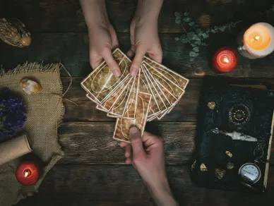 A person holds several tarot cards above a table.